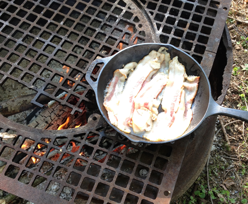 
Cooking meat over a campfire using a grill while camping outdoors
