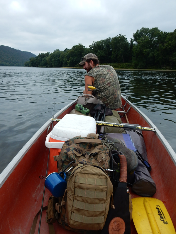 A man boating with carrying military gear, military bags, and fishing gear.
