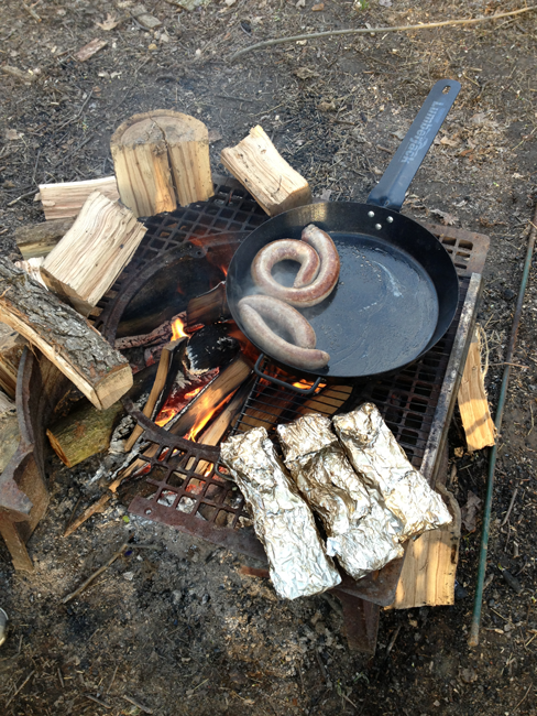 Cooking food over a campfire using a wooden stave.
